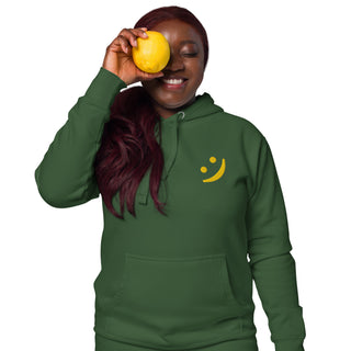 Woman wearing The Happy Channel® Smile Unisex Premium Hoodie in forest green with gold embroidered Smile
