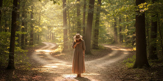 A woman standing at a crossroads facing two divergent paths, both are lit with sunshine softly filtering through trees